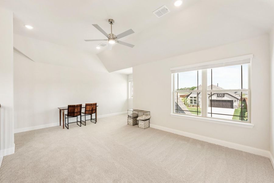 Spacious bonus room with vaulted ceiling, ceiling fan, carpet flooring, and large window overlooking neighborhood