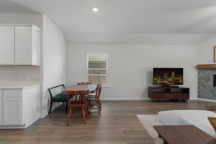 Dining space with baseboards, dark wood-style floors, vaulted ceiling, a fireplace, and recessed lighting