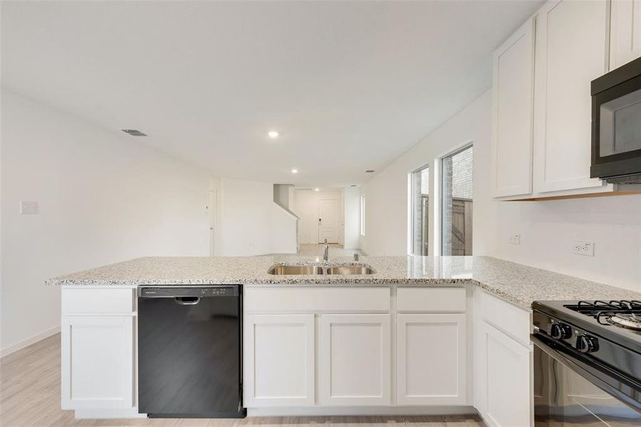 Kitchen featuring sink, light stone counters, black appliances, kitchen peninsula, and white cabinets