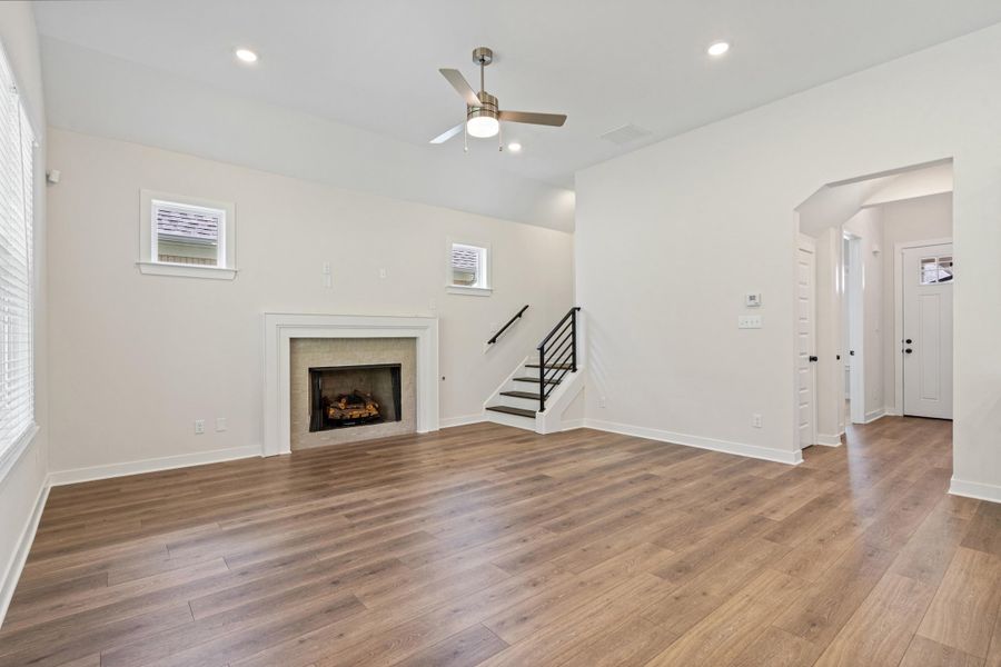 Spacious living area featuring wood-finish flooring, a fireplace with a stone surround and white mantel, and recessed lighting Spacious living area featuring wood-finish flooring, a fireplace with a stone surround and white mantel, and recessed lighting