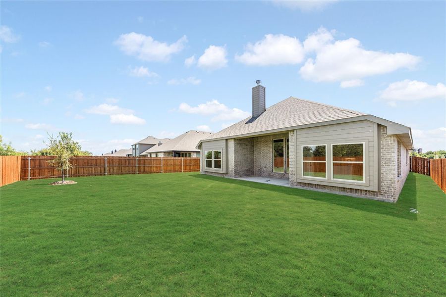 Backyard of brick home with large green lawn, wood privacy fence, and covered patio area