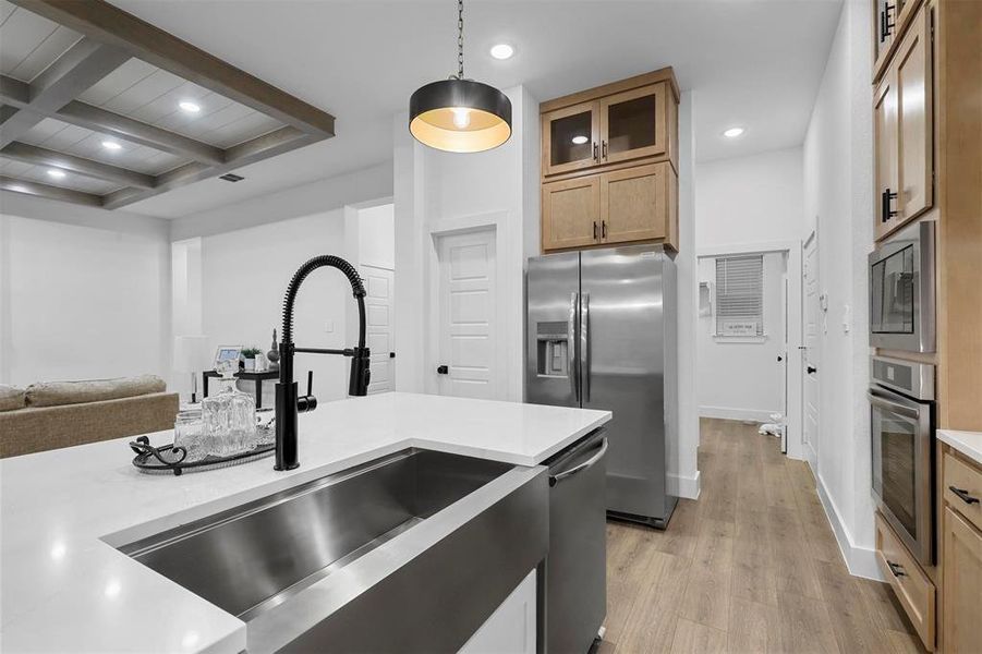 Kitchen with stainless steel appliances, light hardwood / wood-style floors, beamed ceiling, sink, and hanging light fixtures