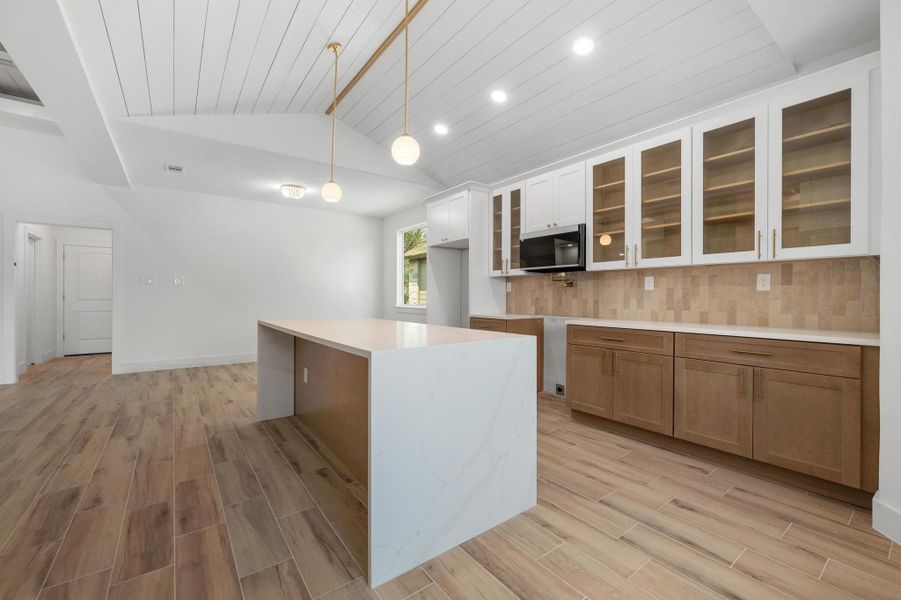 Kitchen featuring glass insert cabinets, decorative backsplash, wood tiled floors, lofted ceiling, and brown cabinets Kitchen featuring glass insert cabinets, decorative backsplash, wood tiled floors, lofted ceiling, and brown cabinets