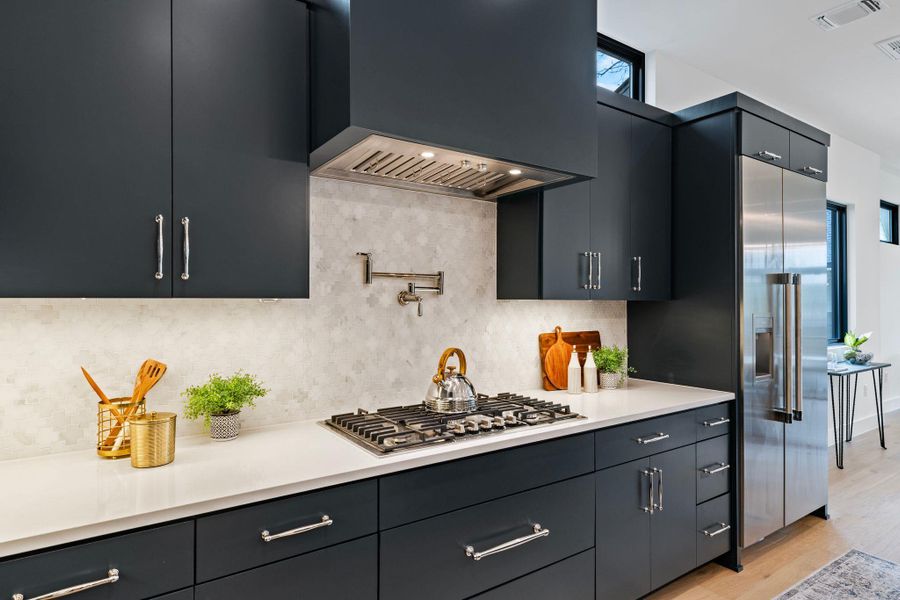 Kitchen featuring custom exhaust hood, stainless steel gas cooktop, backsplash, light countertops, and light wood-type flooring