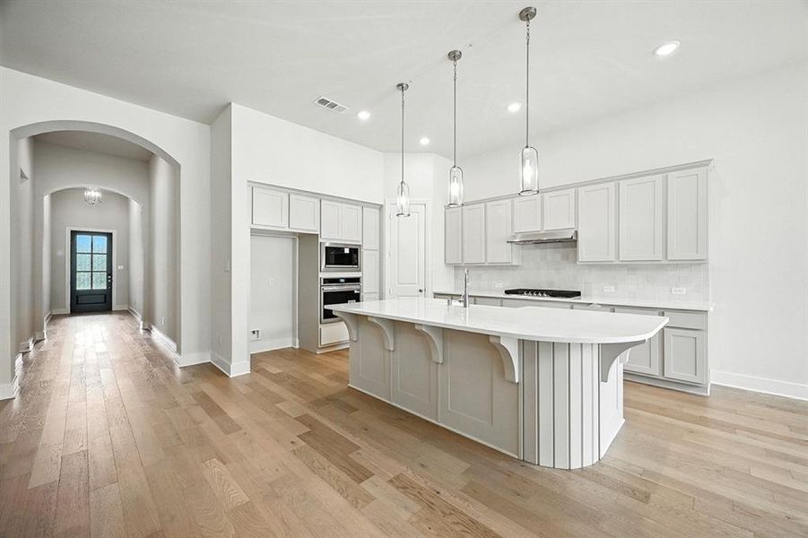 Kitchen featuring arched walkways, backsplash, light wood-style flooring, a breakfast bar area, and recessed lighting Kitchen featuring arched walkways, backsplash, light wood-style flooring, a breakfast bar area, and recessed lighting