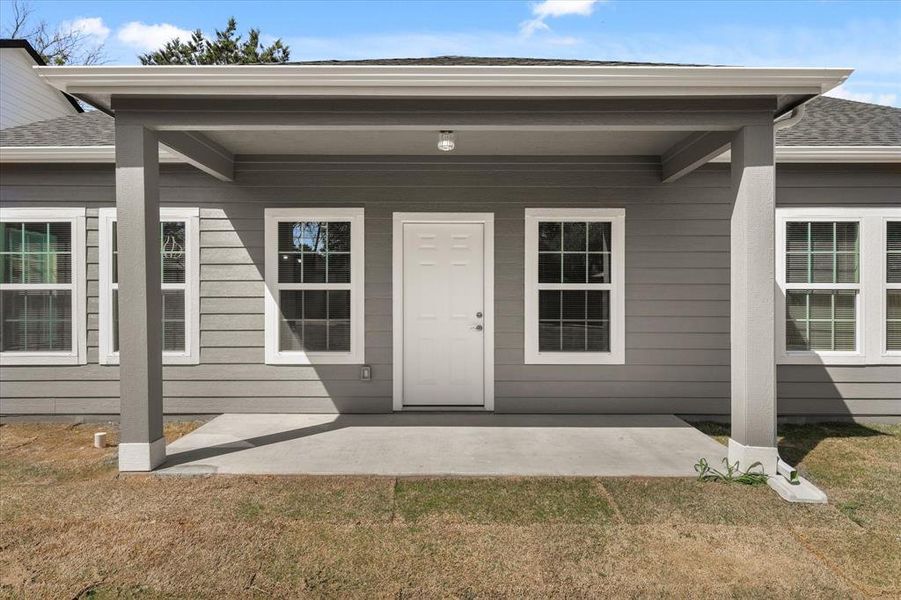 View of exterior entry featuring a patio and a shingled roof