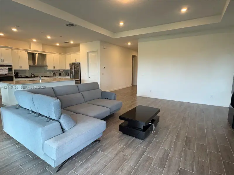 Open-concept interior featuring wood-finish tile flooring, tray ceilings, recessed lighting, white cabinetry, and a stone-topped kitchen island
