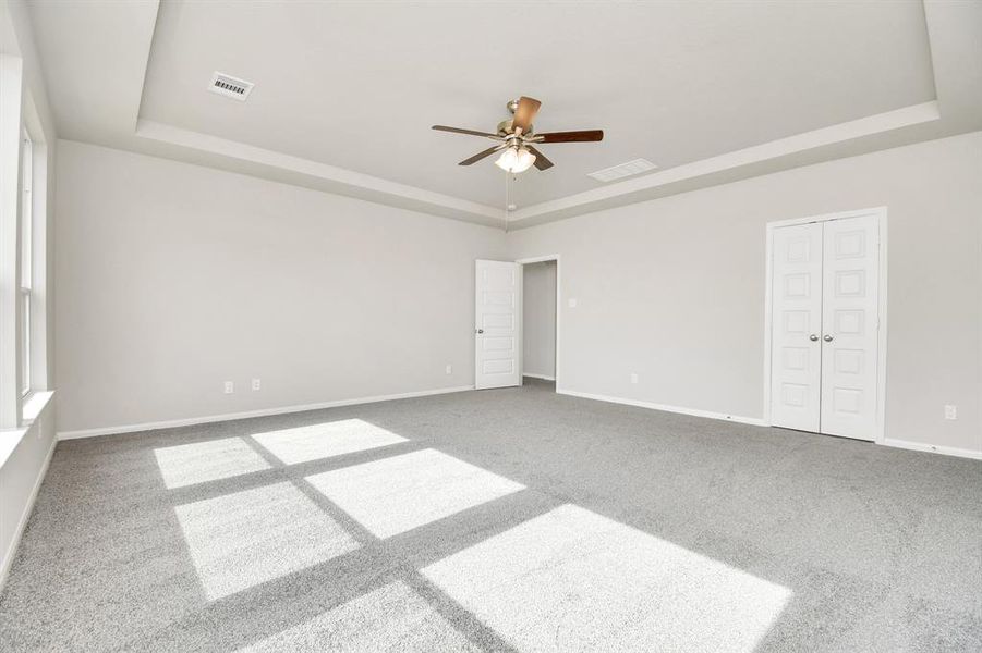 Step into the the primarybedroom with plush carpet, high tray ceiling, ceiling fan, and large windows.