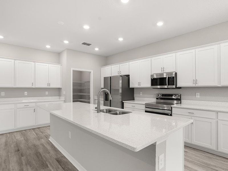 The spacious kitchen wows with a large island, bright lighting, and ample cabinet and counter space - Everly by Highland Homes