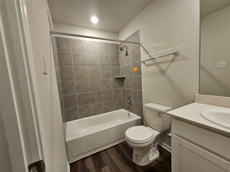 Full bathroom with vanity, a textured wall, shower / bathtub combination with curtain, and dark wood-style flooring Full bathroom with vanity, a textured wall, shower / bathtub combination with curtain, and dark wood-style flooring