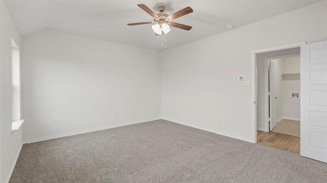 Spacious room featuring vaulted ceilings, light gray carpet, and a ceiling fan with light fixture