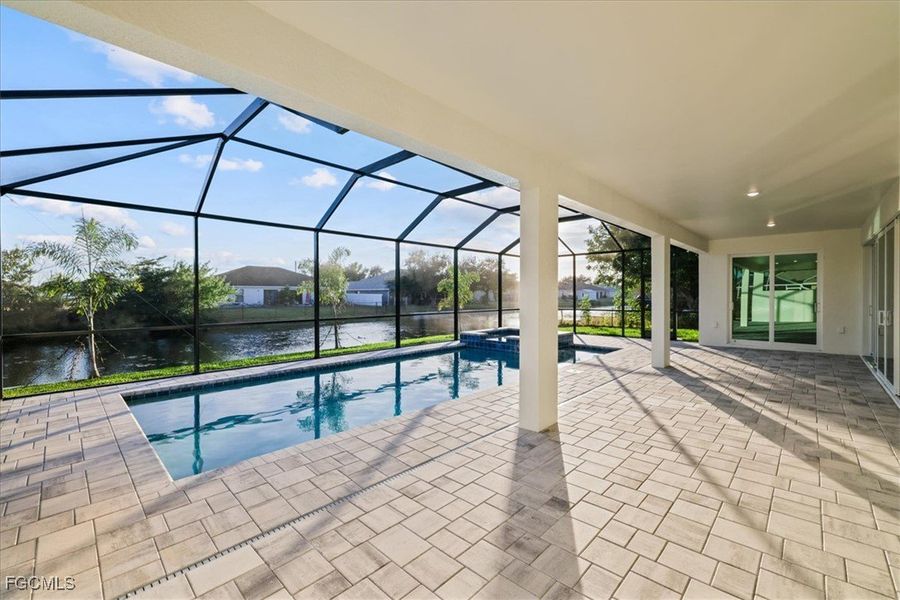 View of swimming pool with a sunroom, glass enclosure, a pool with connected hot tub, a patio area, and a water view