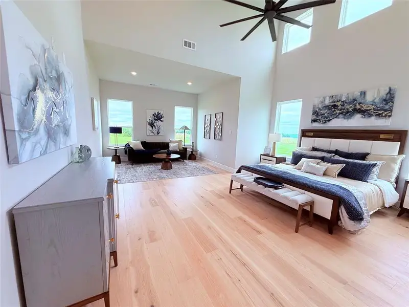 Spacious room featuring light wood-finish flooring, high vaulted ceilings, and a contemporary ceiling fan