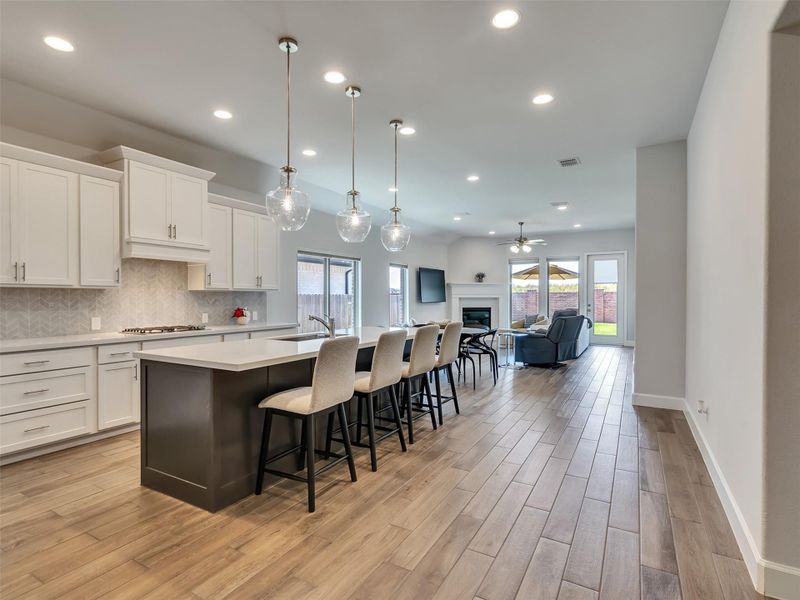 Sleek open-concept kitchen and living area featuring modern pendant lighting, a large island with seating, spacious cabinetry, and a cozy fireplace.