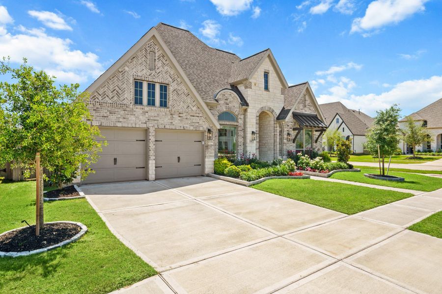 This photo showcases a charming, brick-accented home with a tandem three car garage. The property features a spacious driveway double driveway.