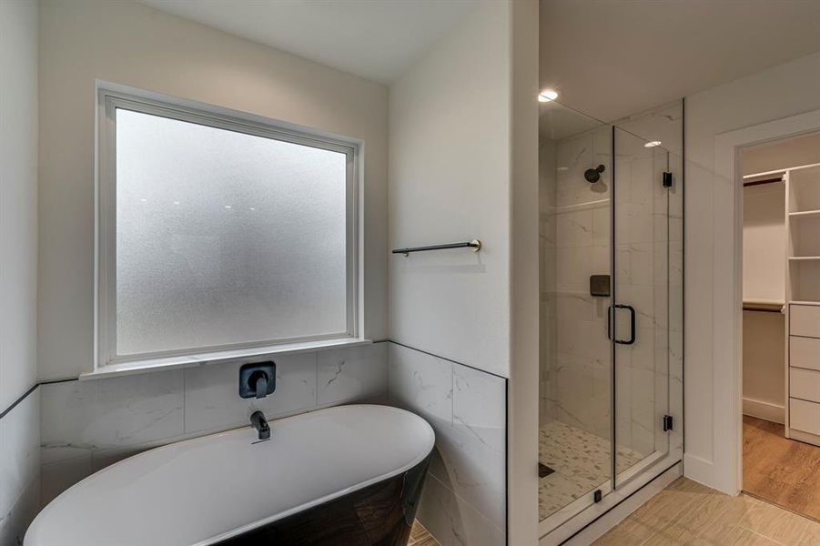 Full bath with a freestanding tub, a spacious closet, a marble finish shower, and wood finished floors