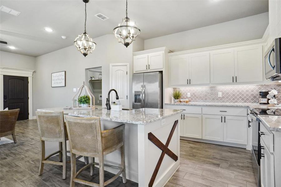 Kitchen featuring decorative backsplash, light stone countertops, an island with sink, stainless steel appliances, and light wood-type flooring