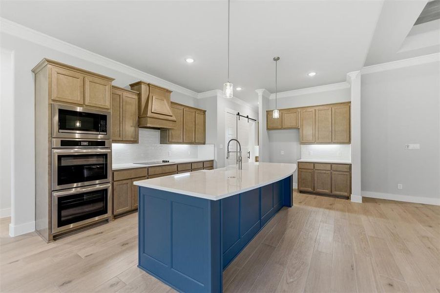 Dual tone kitchen with stainless steel appliances, a barn door, backsplash, an island with sink, and light wood-style flooring