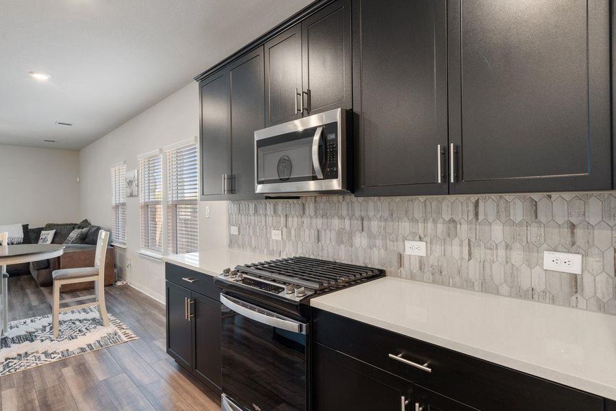 Modern kitchen with sleek dark cabinetry, stainless steel appliances, gas range, and stylish tile backsplash. Modern kitchen with sleek dark cabinetry, stainless steel appliances, gas range, and stylish tile backsplash.