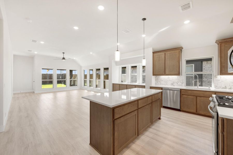 Open kitchen with large island, brown cabinets, white countertops, and light wood floors flowing into living area
