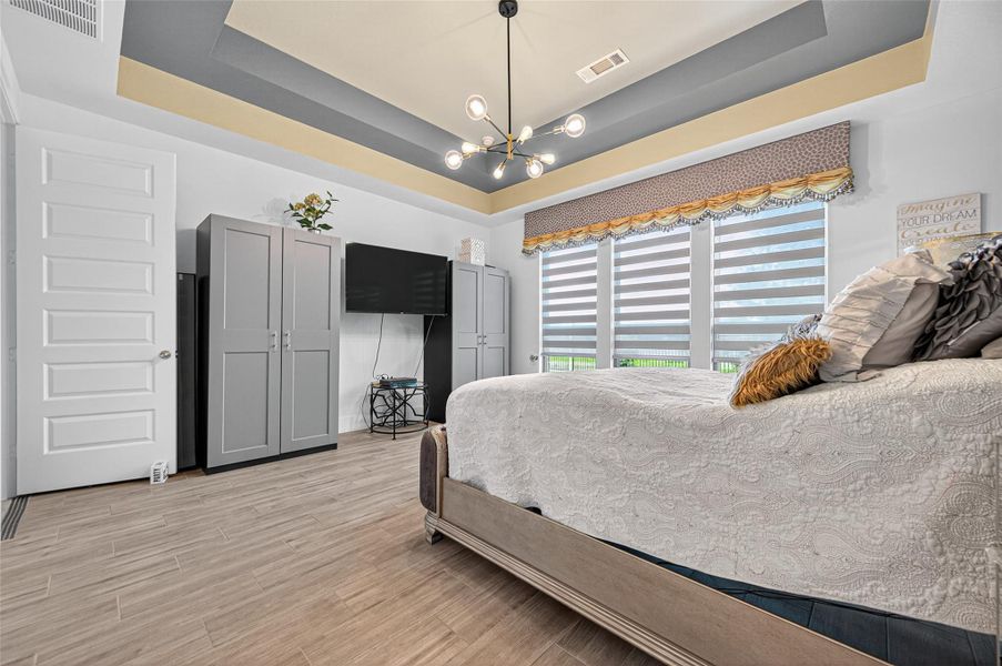 This bedroom features a modern design with a tray ceiling and stylish light fixture. It has large windows with dual shades for natural light control, and ample storage with sleek gray cabinets. The room combines elegance and functionality, offering a cozy yet contemporary feel. This bedroom features a modern design with a tray ceiling and stylish light fixture. It has large windows with dual shades for natural light control, and ample storage with sleek gray cabinets. The room combines elegance and functionality, offering a cozy yet contemporary feel.