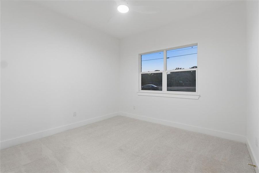 Spacious room featuring light-colored carpeting, a bright window with white trim, white walls, and a ceiling-mounted fan with integrated lighting