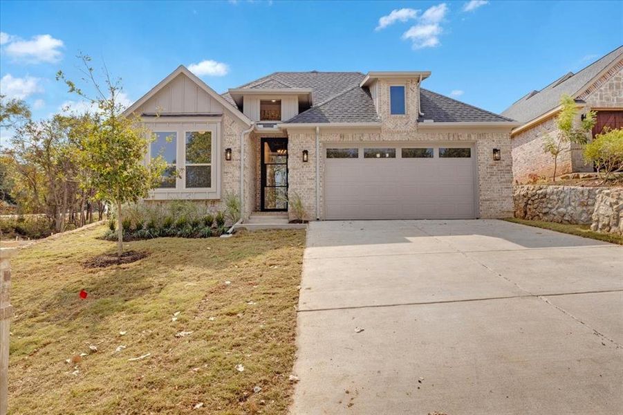 View of front of property featuring a front lawn, board and batten siding, driveway, brick siding, and a shingled roof