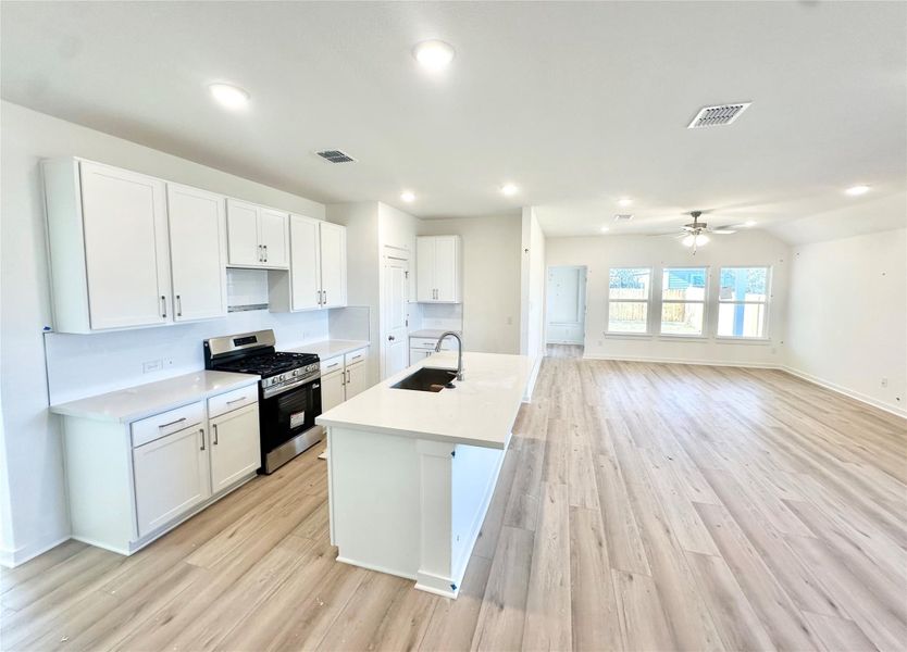 Kitchen featuring gas stove, white cabinets, light wood-style flooring, a center island with sink, and ceiling fan