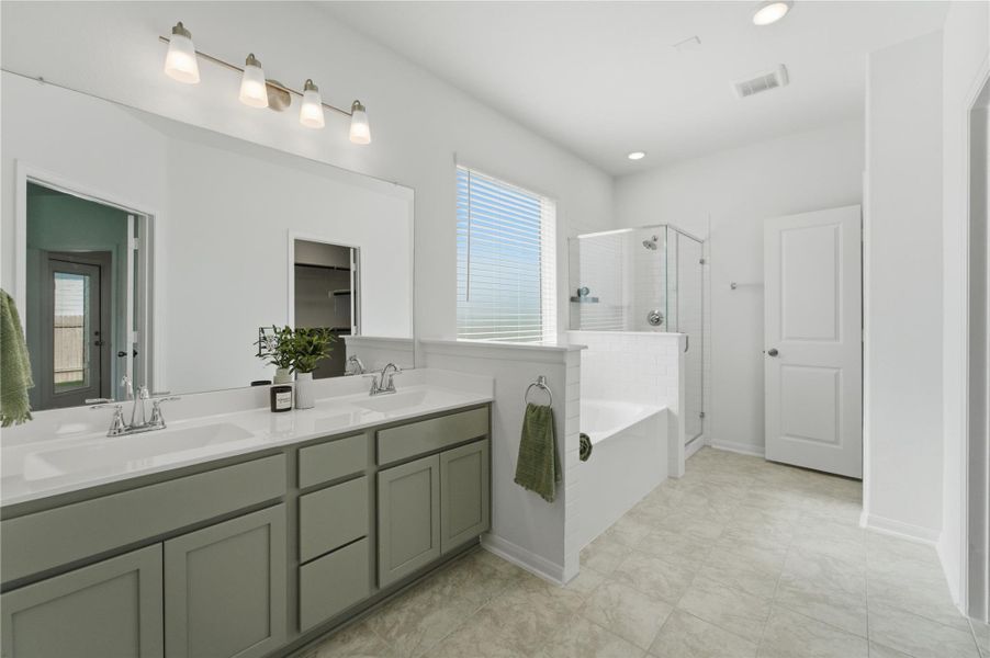 A well-lit primary bathroom provides a dual vanity, a soaking tub, and a separate glass-enclosed shower. A well-lit primary bathroom provides a dual vanity, a soaking tub, and a separate glass-enclosed shower.