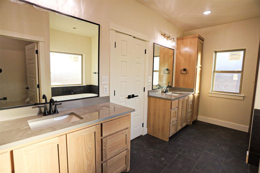 Bathroom featuring two vanities, a bath, dark tile patterned floors, and recessed lighting