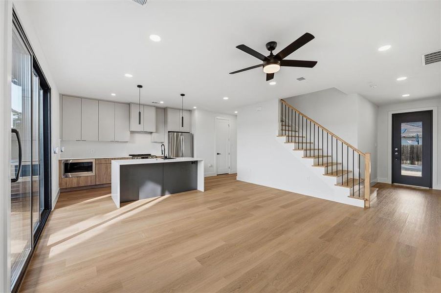 Living Room features recessed lighting and ceiling fan with light fixture. Large window and sliding glass door provide abundant natural light and backyard views. Open-concept layout connects directly to the kitchen island. Vinyl flooring extends throughout.