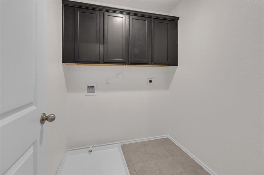 This is a clean, modern laundry room with dark cabinetry above washer and dryer hookups, set against a neutral color scheme with tile flooring.