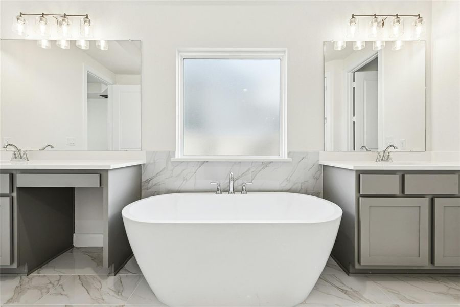 Bathroom featuring two vanities, tile walls, wainscoting, light marble finish floors, and a freestanding tub