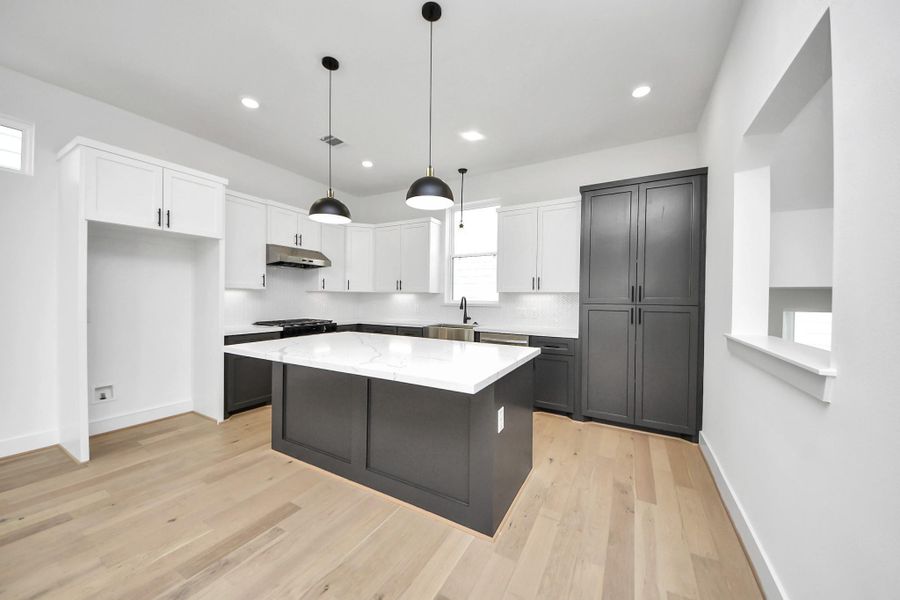Chefs open kitchen and living space features stainless steel appliances, a modern island with a sink, quartz countertops, and custom black matte pendant lighting.
