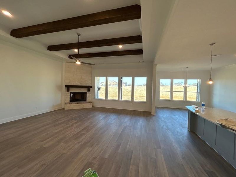 Unfurnished living room featuring a brick fireplace, dark wood-type flooring, recessed lighting, plenty of natural light, and beamed ceiling