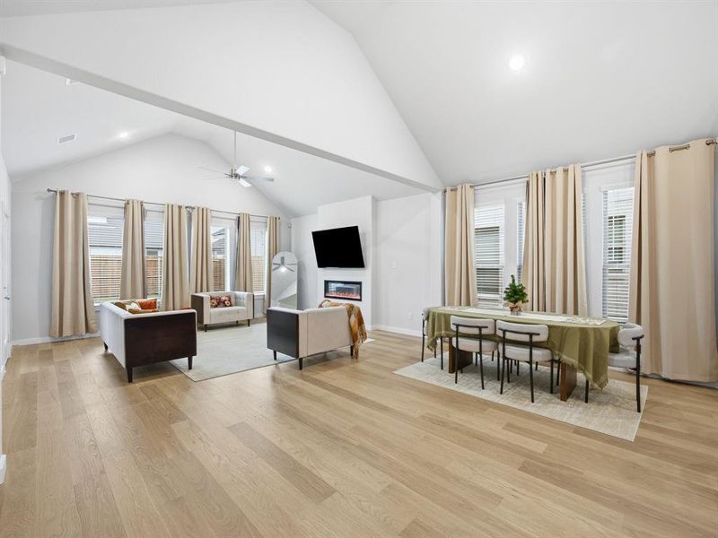 Living area featuring plenty of natural light, recessed lighting, light wood-style flooring, high vaulted ceiling, and a glass covered fireplace