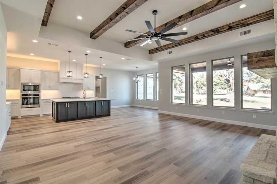 Unfurnished living room with ceiling fan with notable chandelier, beam ceiling, light wood-type flooring, and sink