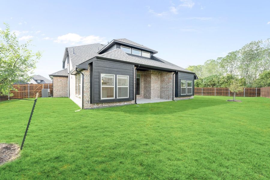 Rear view of brick and dark siding home with large green backyard and wood privacy fence