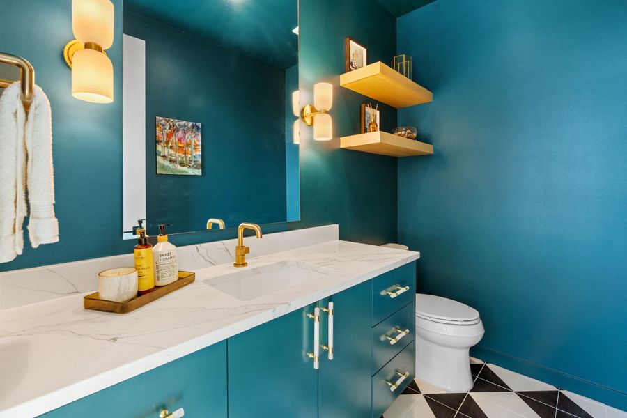 Bathroom vanity featuring a white countertop with integrated sink, gold-finish faucet, and teal cabinetry with gold-finish hardware