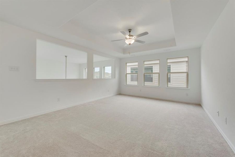 Empty room featuring a tray ceiling, ceiling fan, and light colored carpet