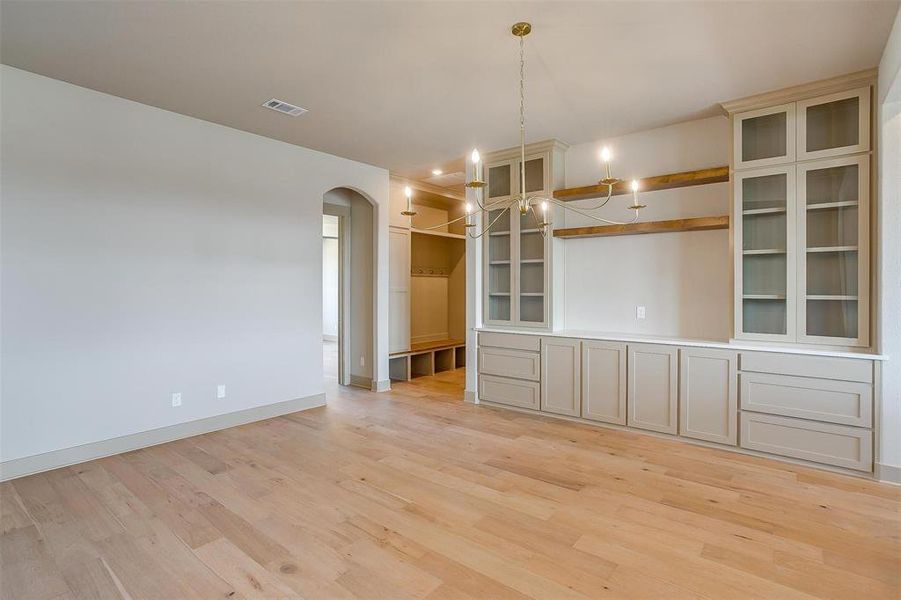 Unfurnished dining area with baseboards, light wood-type flooring, arched walkways, and an inviting chandelier