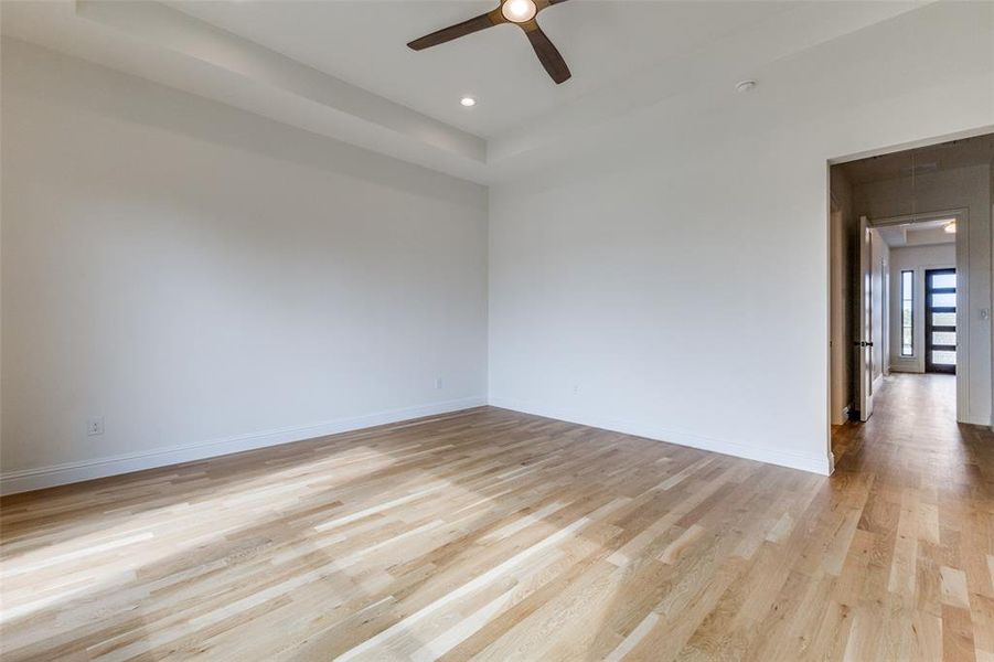 Spare room with light wood-style flooring, a ceiling fan, baseboards, a tray ceiling, and recessed lighting