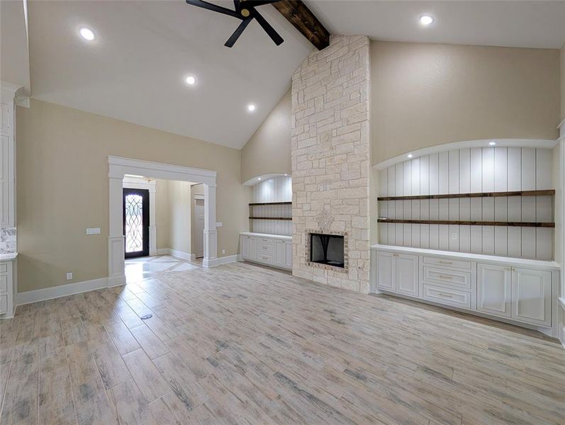 Unfurnished living room with light wood-style floors, beamed ceiling, high vaulted ceiling, a ceiling fan, and a stone fireplace