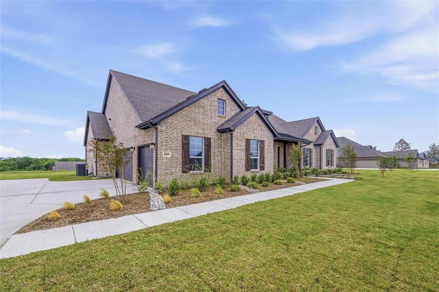 This property features a brick exterior with dark trim and shutters, a well-maintained lawn, and a concrete driveway