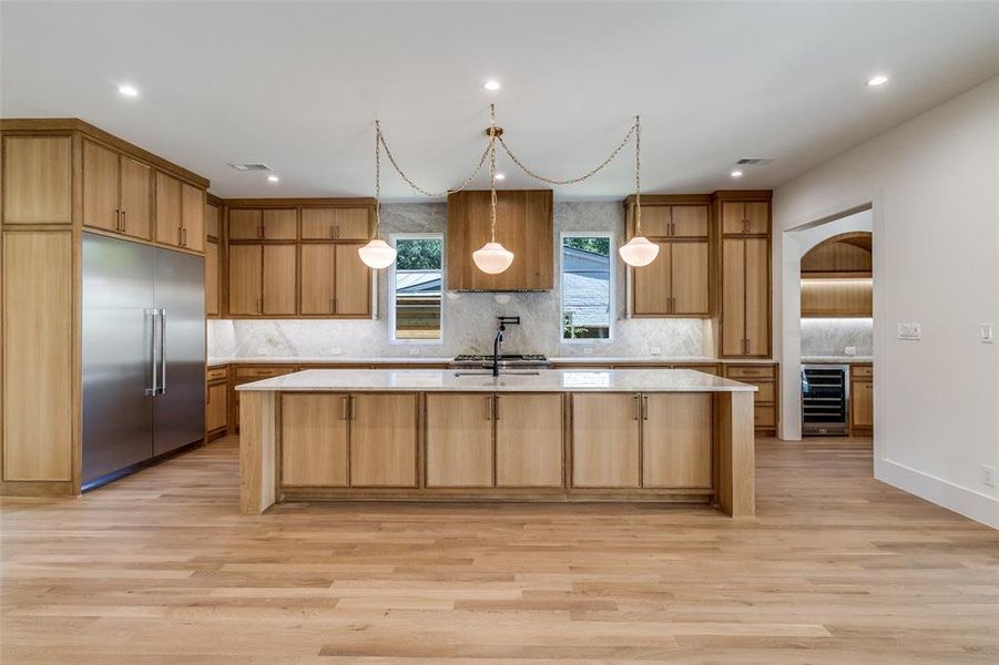 Kitchen featuring decorative backsplash, arched walkways, a large island, light wood-style flooring, and light stone counters Kitchen featuring decorative backsplash, arched walkways, a large island, light wood-style flooring, and light stone counters