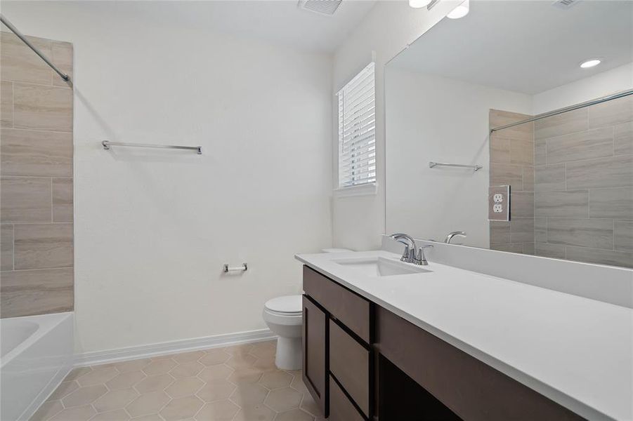 Secondary bath features tile flooring, bath/shower combo with tile surround, stained wood cabinets, beautiful light countertops, mirror, sleek fixtures and modern finishes.