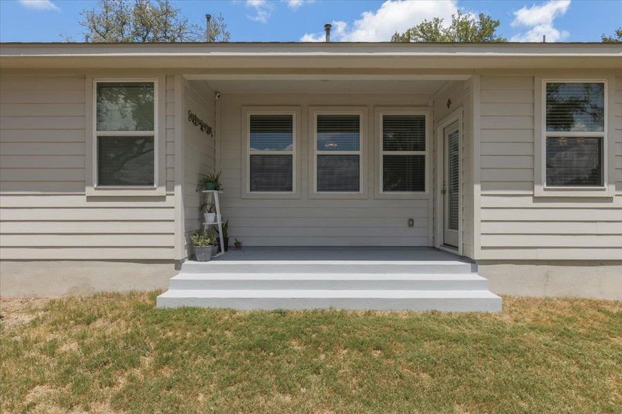 Concrete steps lead up to a shaded back porch framed by horizontal siding.