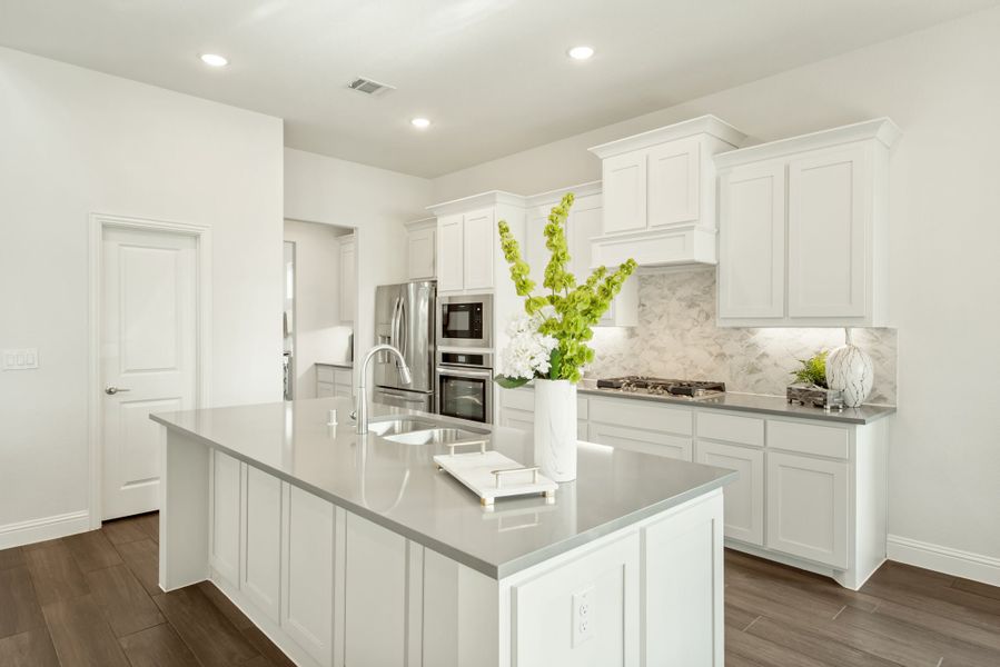 White kitchen with center island, gray countertops, marble backsplash, and stainless steel appliances on dark hardwood floors