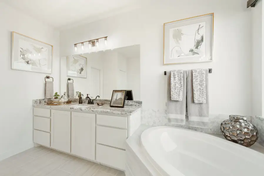 Bathroom with white double vanity, granite countertop, large mirror, and soaking tub with marble surround