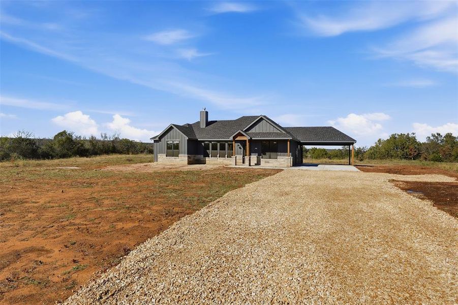 Modern farmhouse style home with a chimney, gravel driveway, a carport, covered porch, and board and batten siding Modern farmhouse style home with a chimney, gravel driveway, a carport, covered porch, and board and batten siding